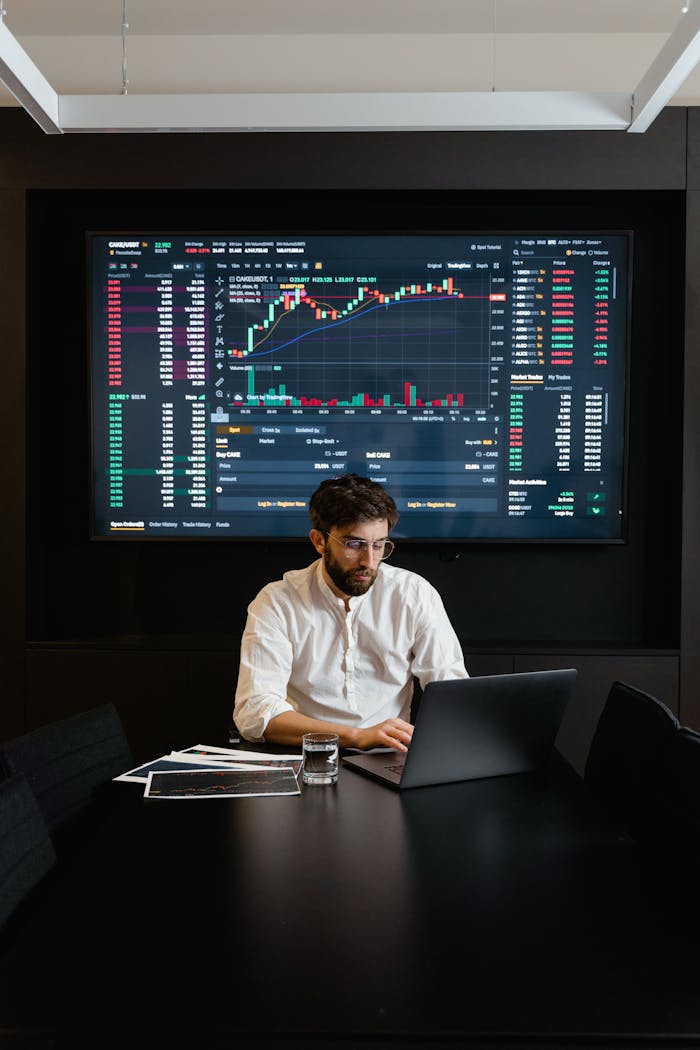 A stock trader analyzes cryptocurrency data on a laptop with graphs and charts on a screen.